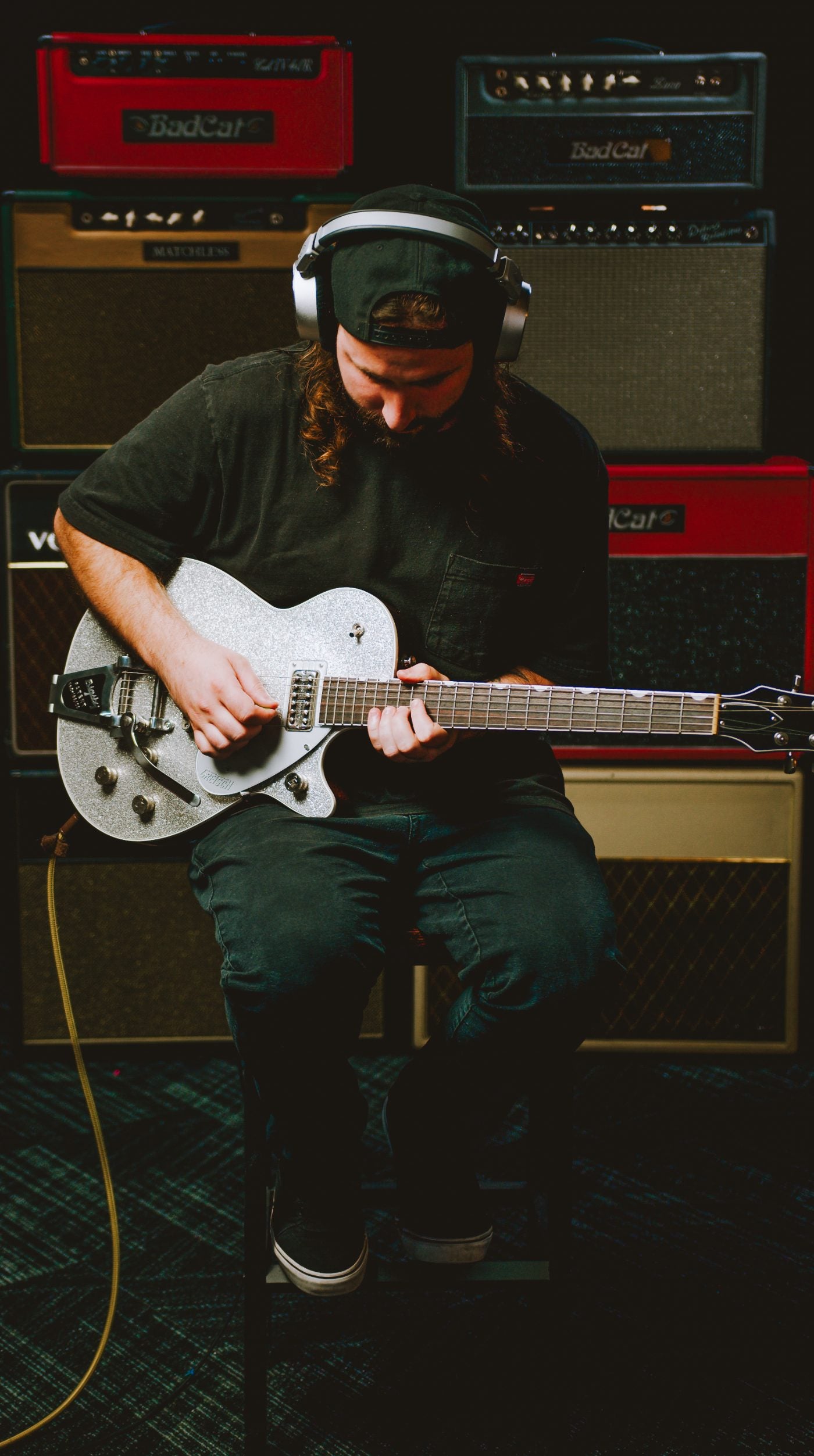 Jamie playing a silver Gretsch in front of a wall of tube amps
